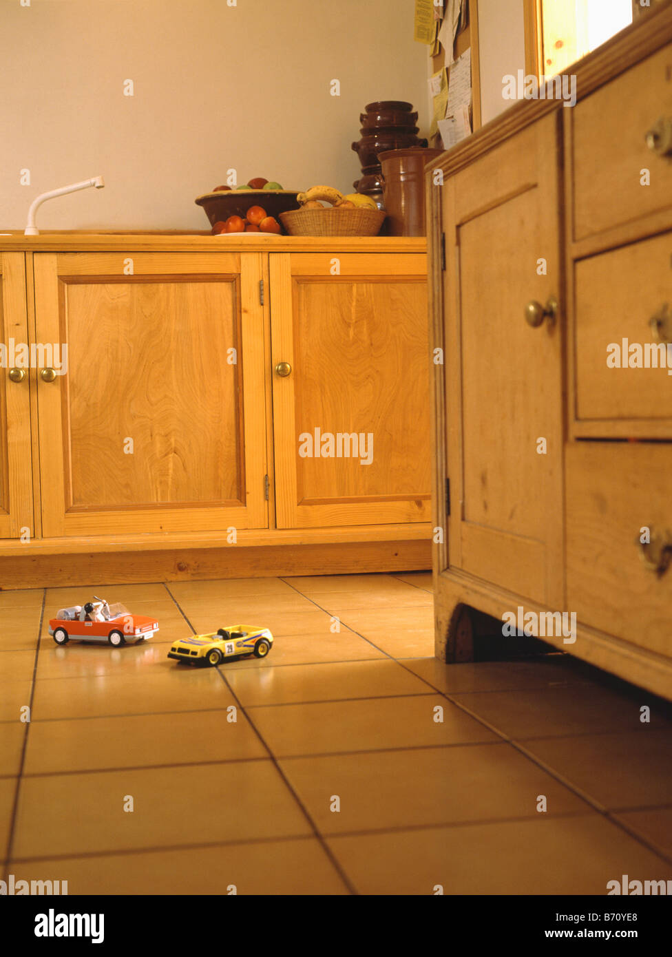 Toy cars on tiled floor of country kitchen with pine cupboard and