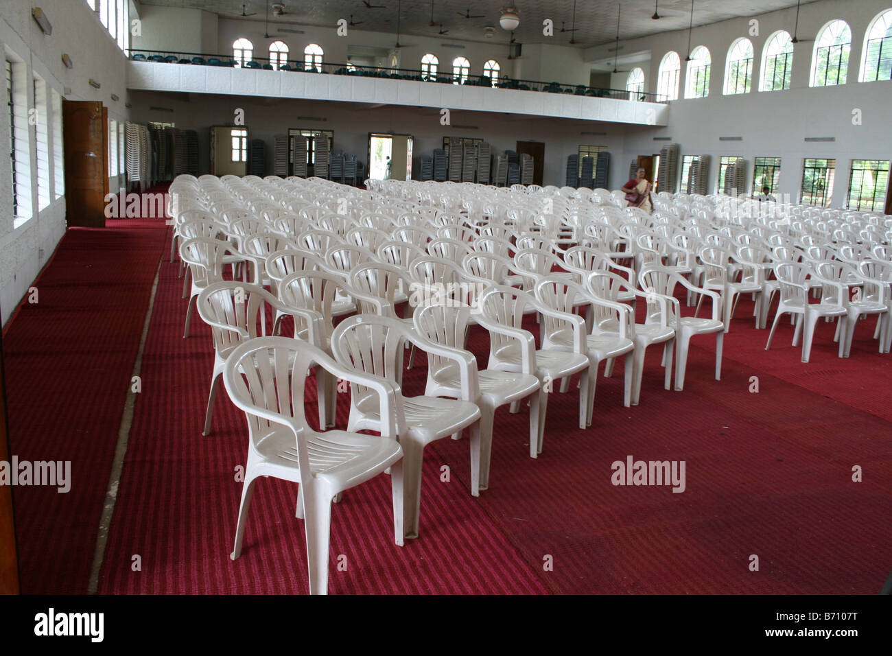 Large number of white color chairs on red carpet arranged for important public function or meeting in a huge hall with balcony Stock Photo
