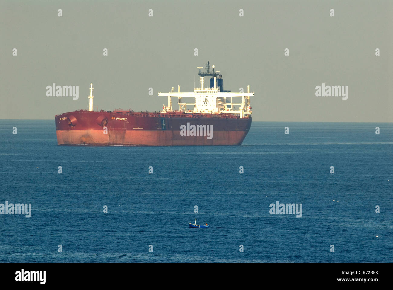 Super tanker anchored in Mediterranean with small open fishing boat in foreground Stock Photo