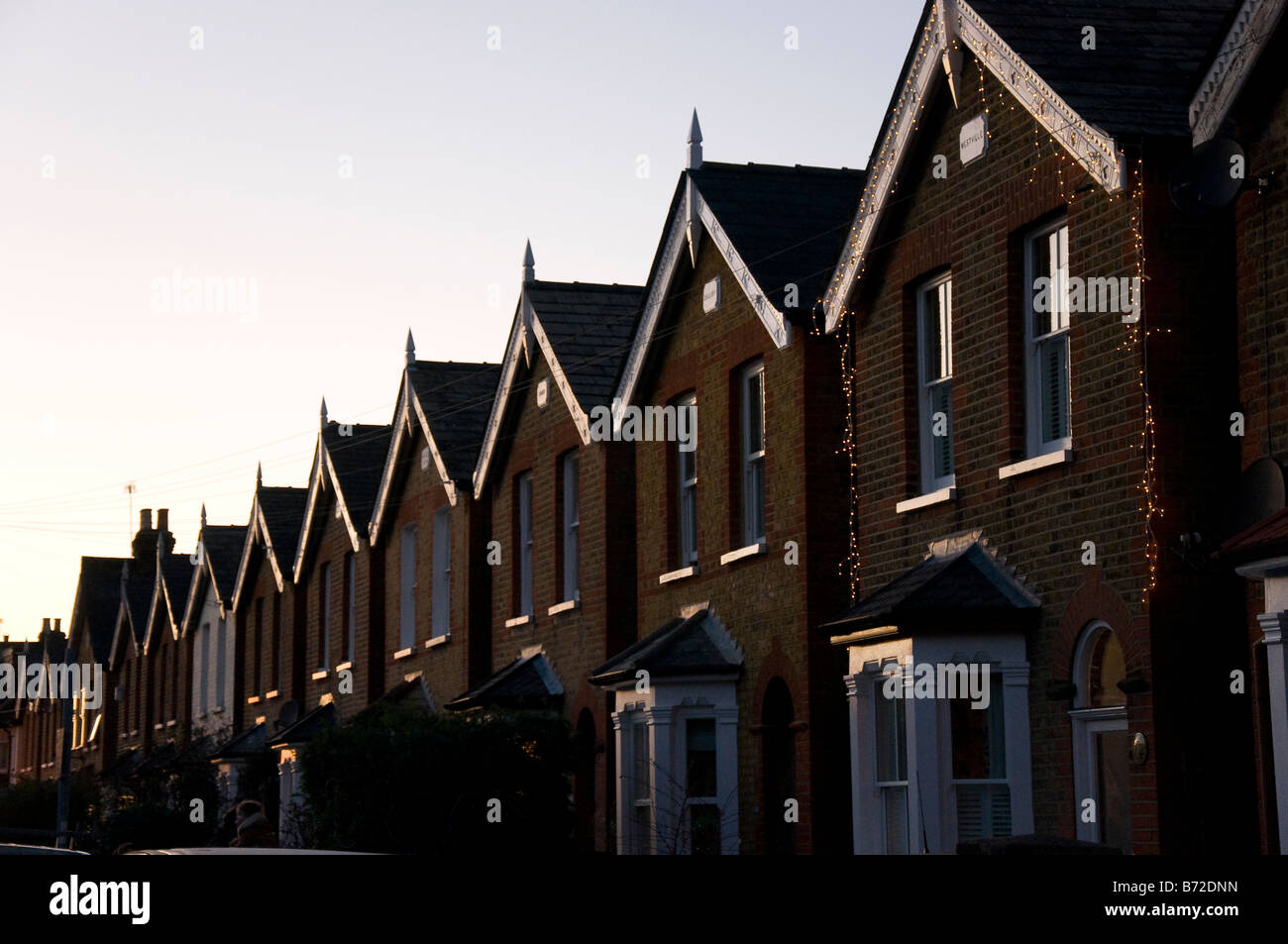 Evening light reflected in the windows and eaves of a row of detached houses on a UK street christmas lights on one house Stock Photo