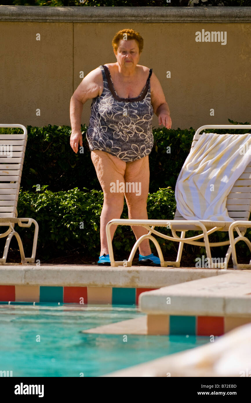 Palm Beach Shores , mature middle aged large portly lady in swimming costume & beach shoes walks towards pool Stock Photo