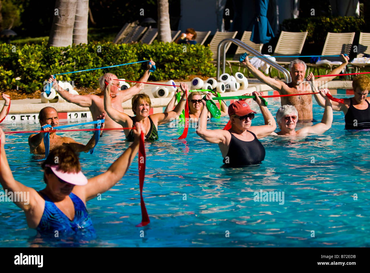 Palm Beach Shores , mature smiling middle aged large men & women in swimming pool do aqua aerobics with elastic stretch strips Stock Photo