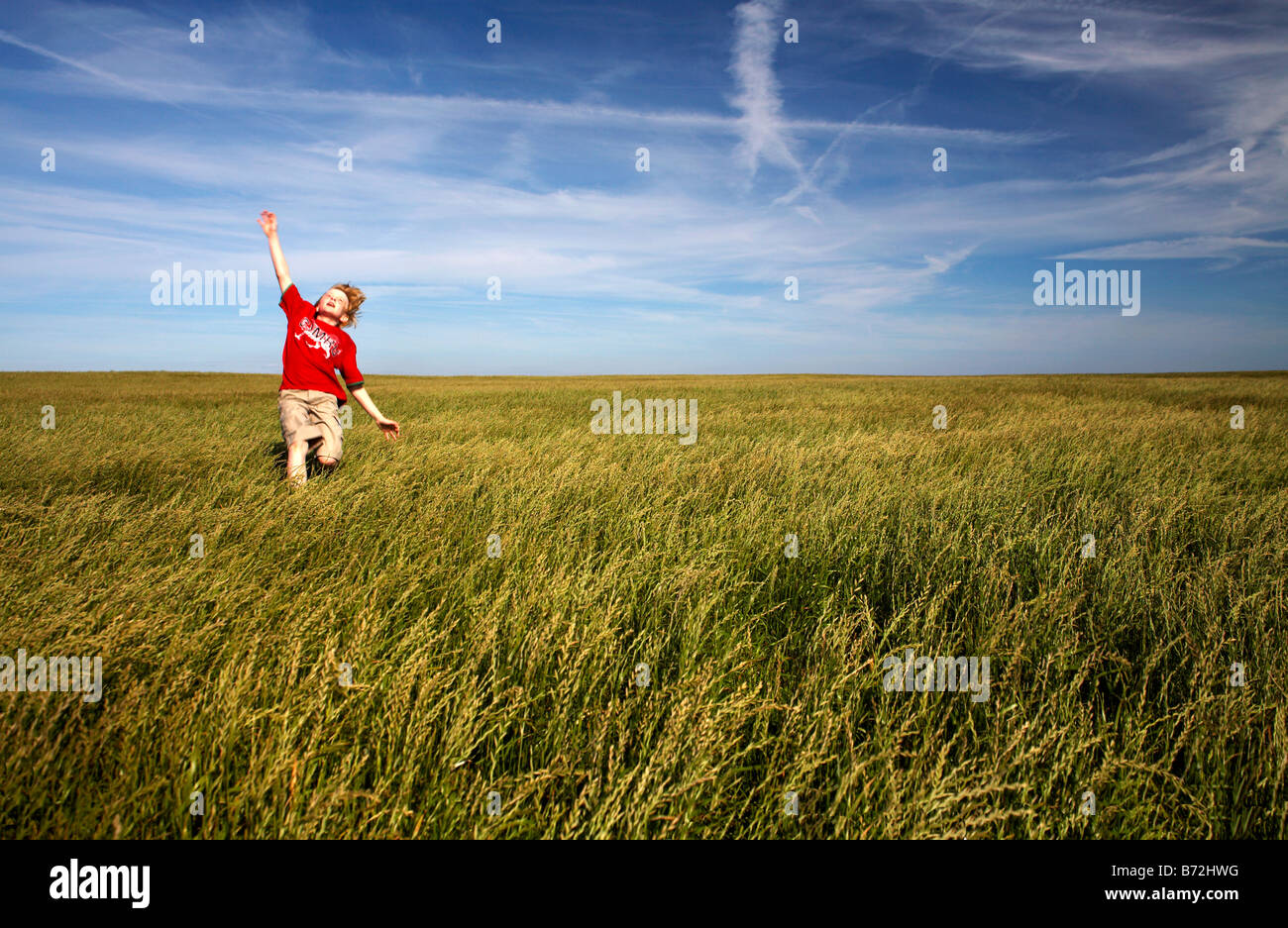 Young boy running through a field of grass in a Cymru T Shirt Glamorgan Heritage coastal path near Nash Point South Wales Stock Photo