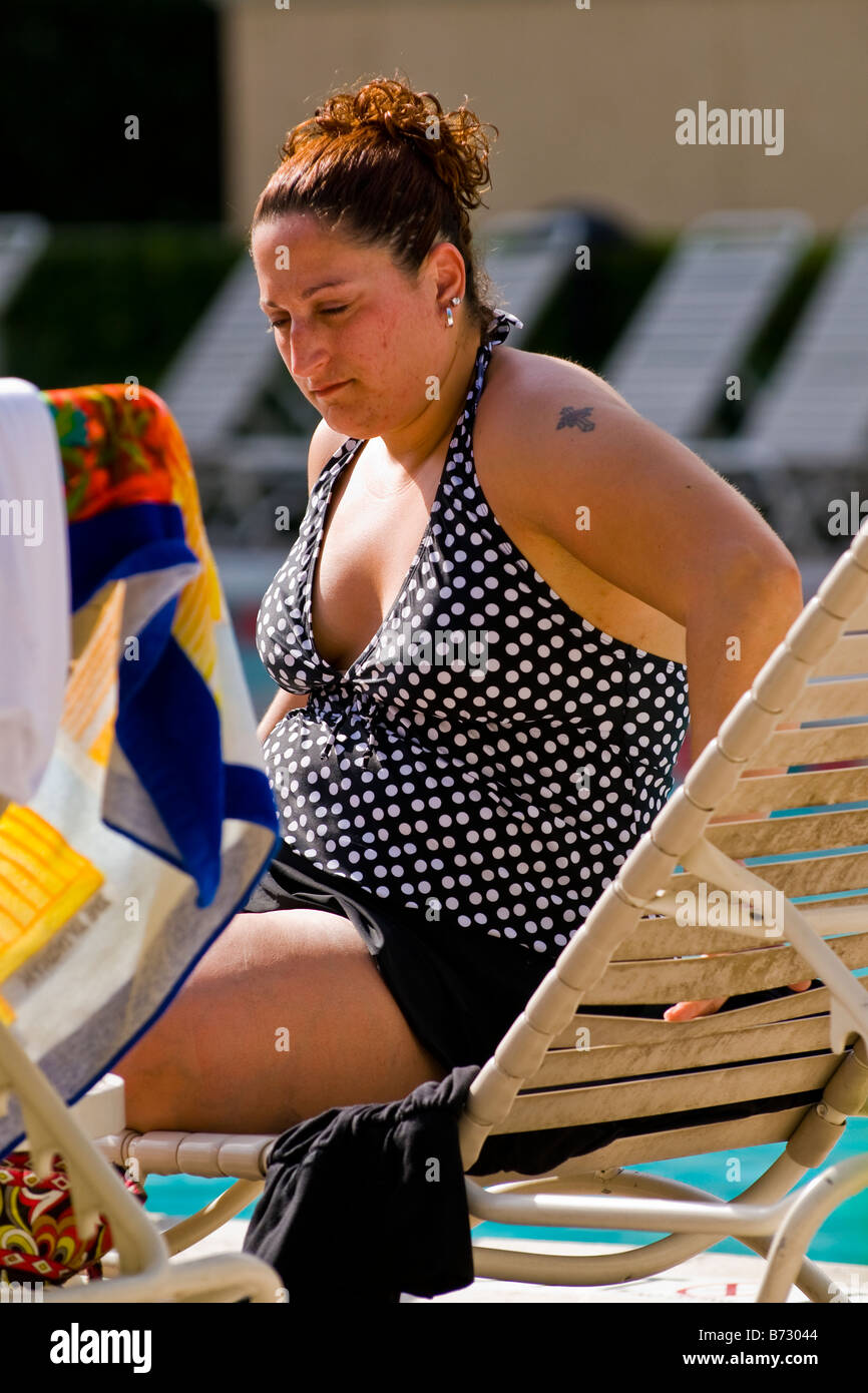 Palm Beach Shores , middle aged large portly lady with tattoo in swimming costume on sun lounger sunbathing by pool Stock Photo