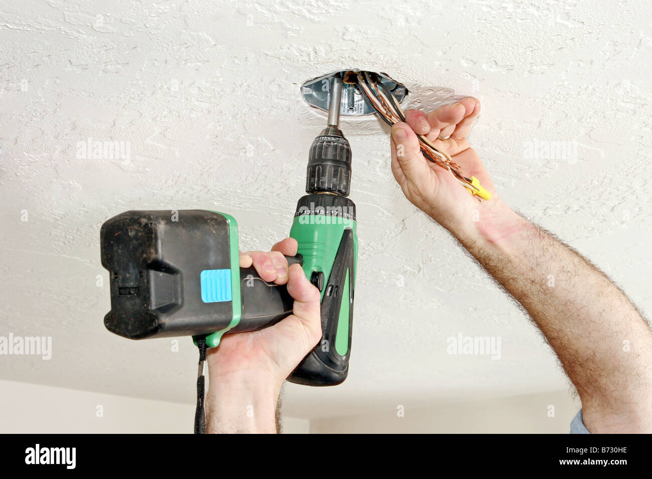 An Electrician S Hands Using A Drill To Screw A Fan Box Into