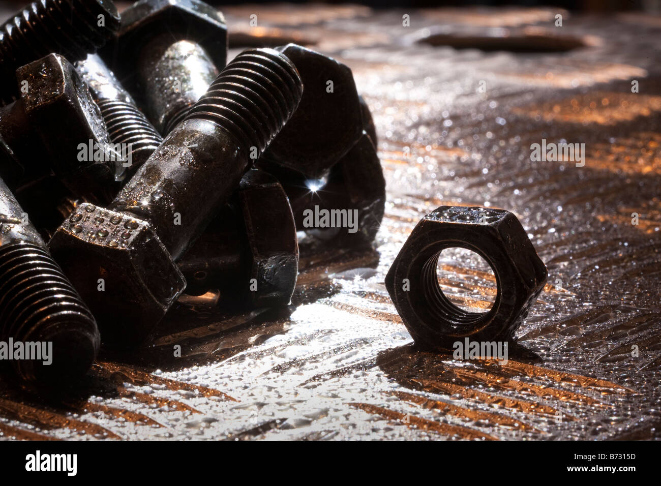 Random artistic pile of threaded bolts and a  hexagonal nut on a sheet steel, backlit, Stock Photo