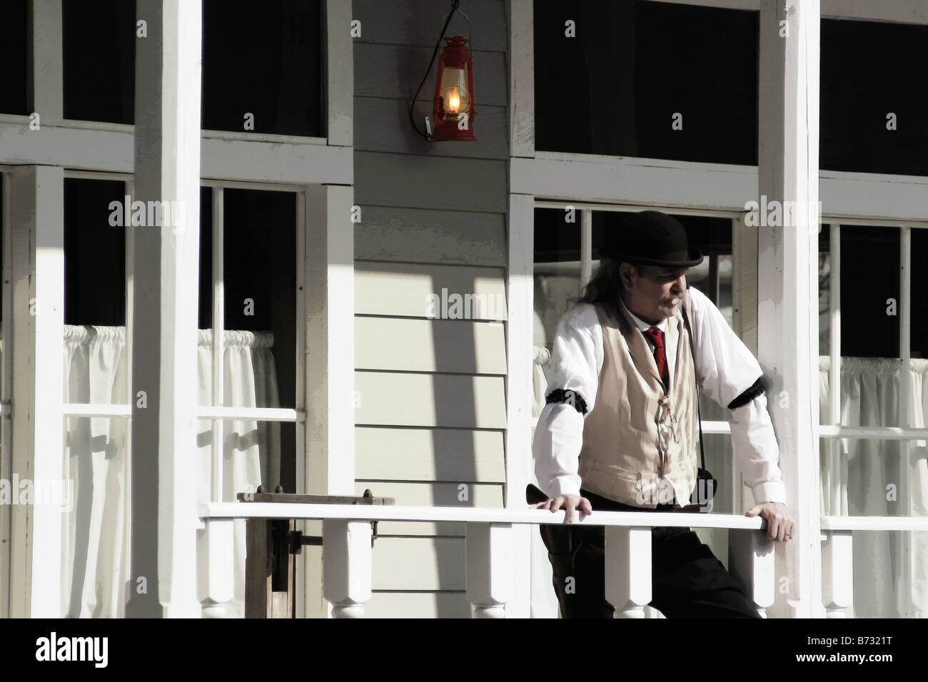 A bar tender from the old western building is outside on the porch taking a break Red tie and lantern digital color Stock Photo