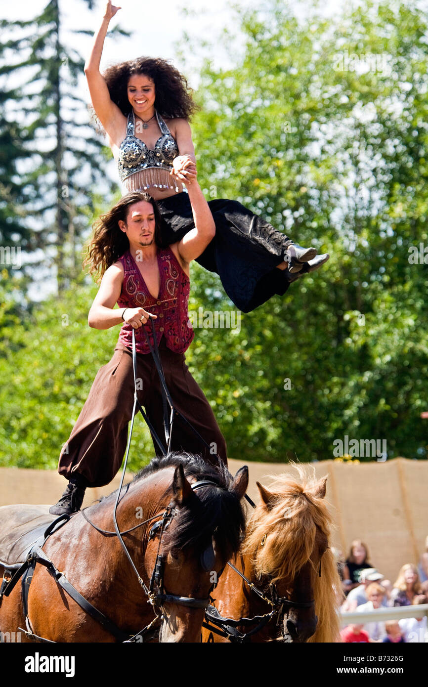 Image of a Gypsy man riding two horses at the same time standing up with a woman on his shoulder
