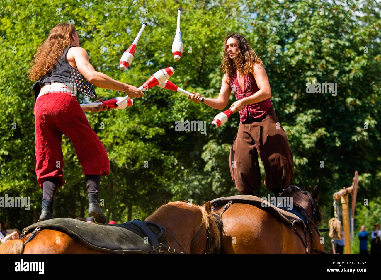 Image of two gypsy men standing up on the backs of horses while juggling with bowling pins Stock Photo