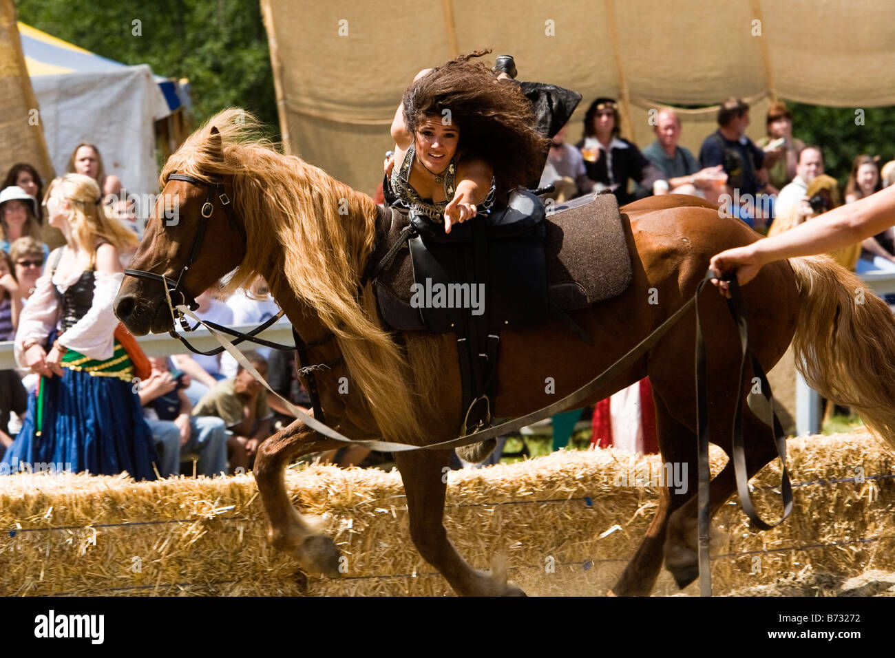 Image of a woman riding laying across the back of a horse pointing directly at the camera Stock Photo