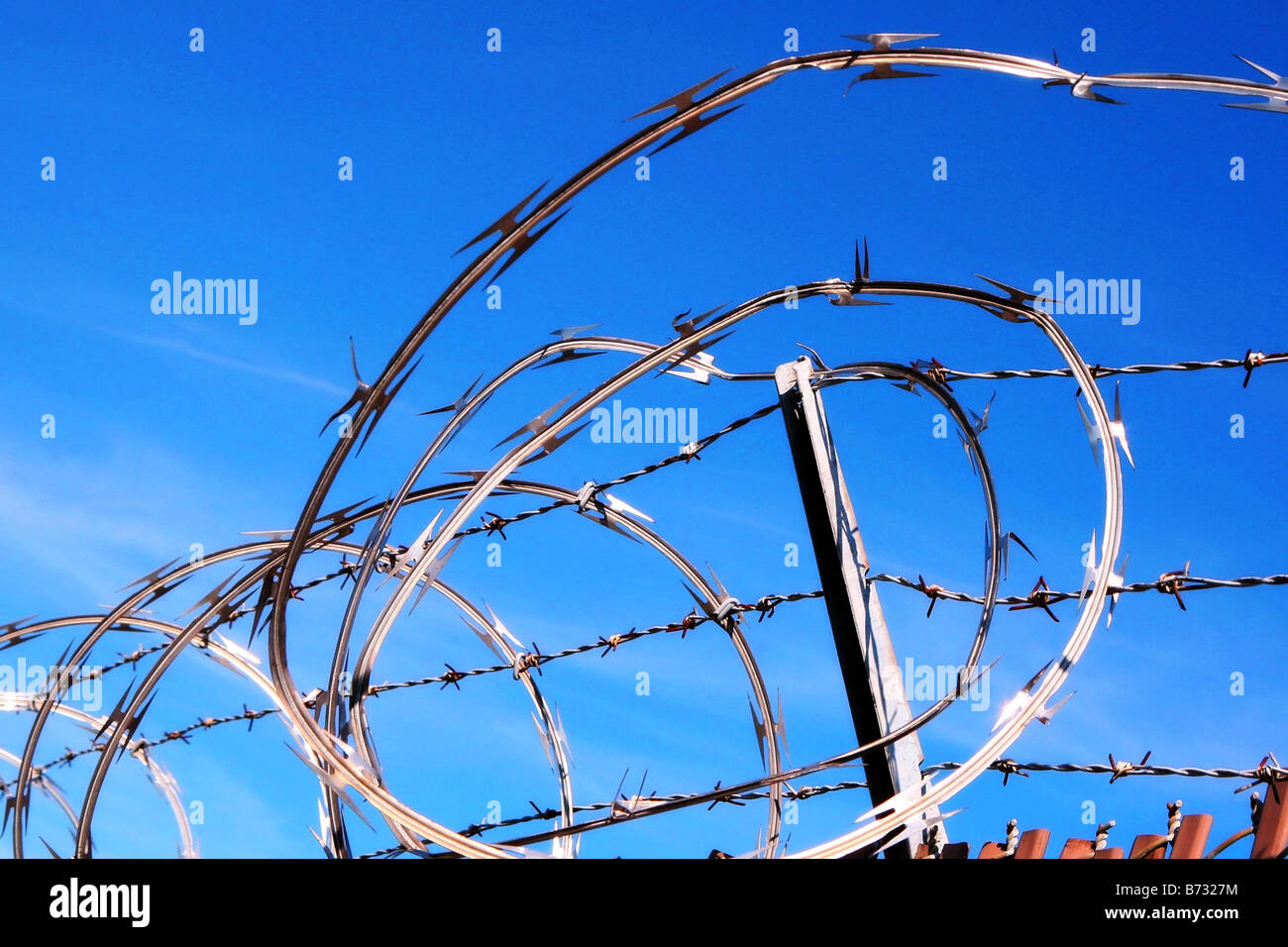 Image of loops of brightly sparkling brand new razor wire set against a beautiful blue sky Stock Photo