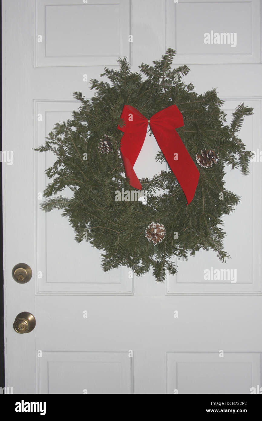 A Christmas wreath hanging on the white front door of a home Red bow Stock Photo