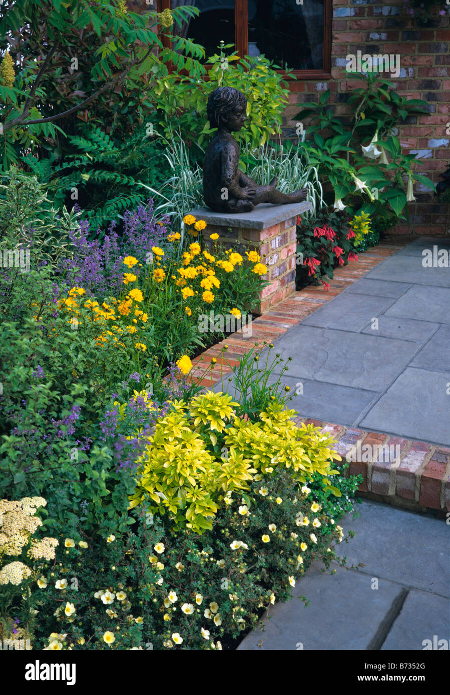 Mixed colourful border with bronze sculpture of seated child in a terrace garden Stock Photo