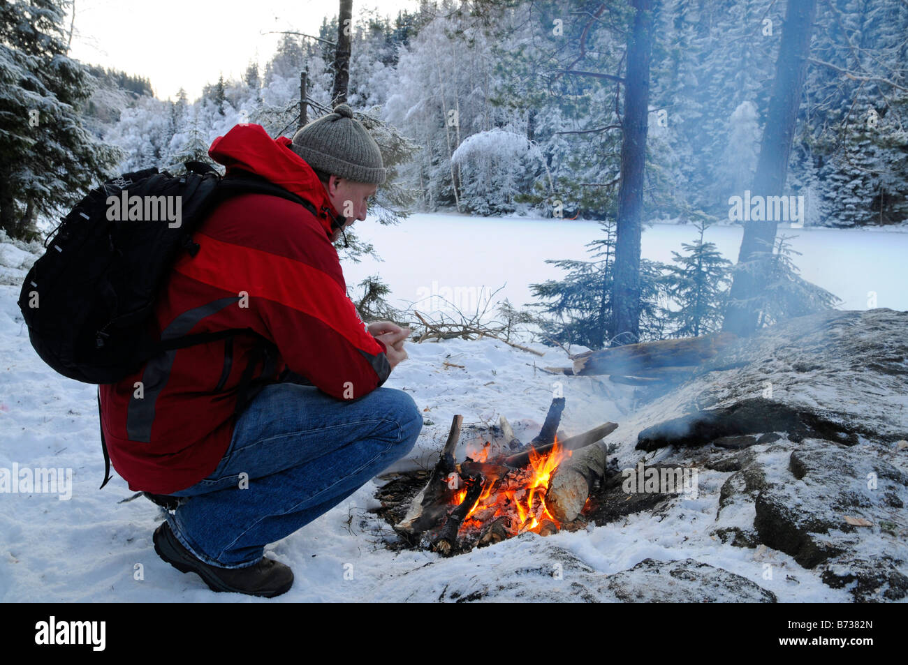 Man warms up crouching by camp fire in snow and cold near Oslo Norway Stock Photo