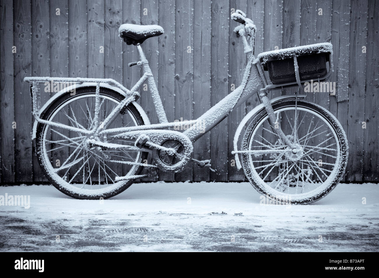 A british royal mail postal delivery bicycle leaning up against a fence on a snowy winters morning. Stock Photo