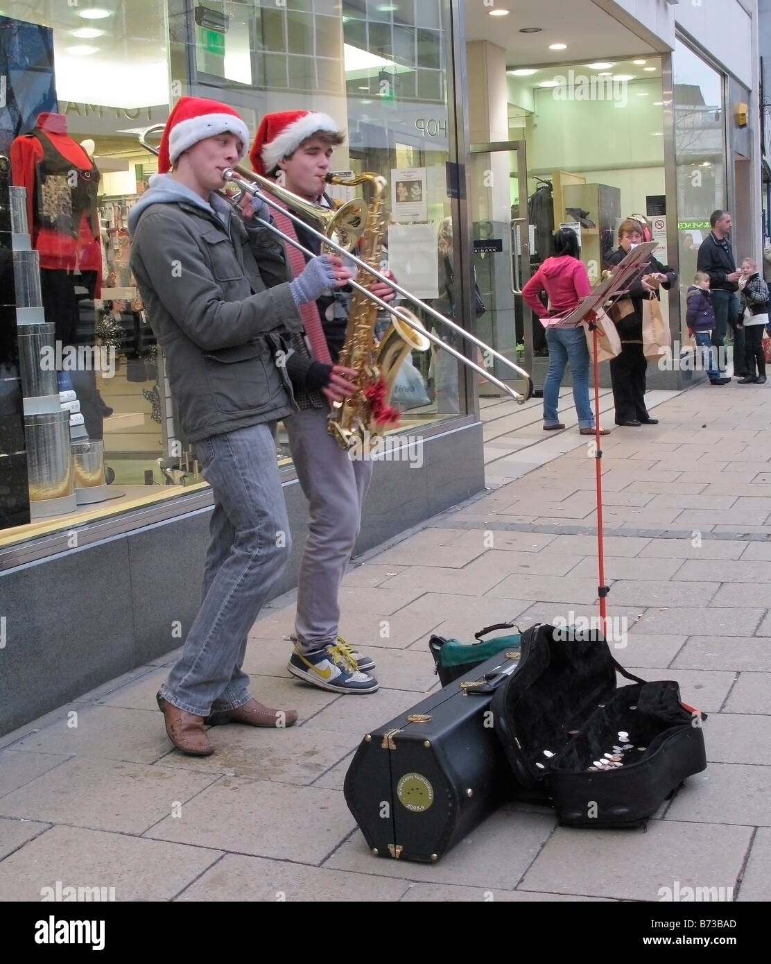 Two lads busking money by playing Christmas carols on trombones on the Street of Norwich during Christmas period Stock Photo