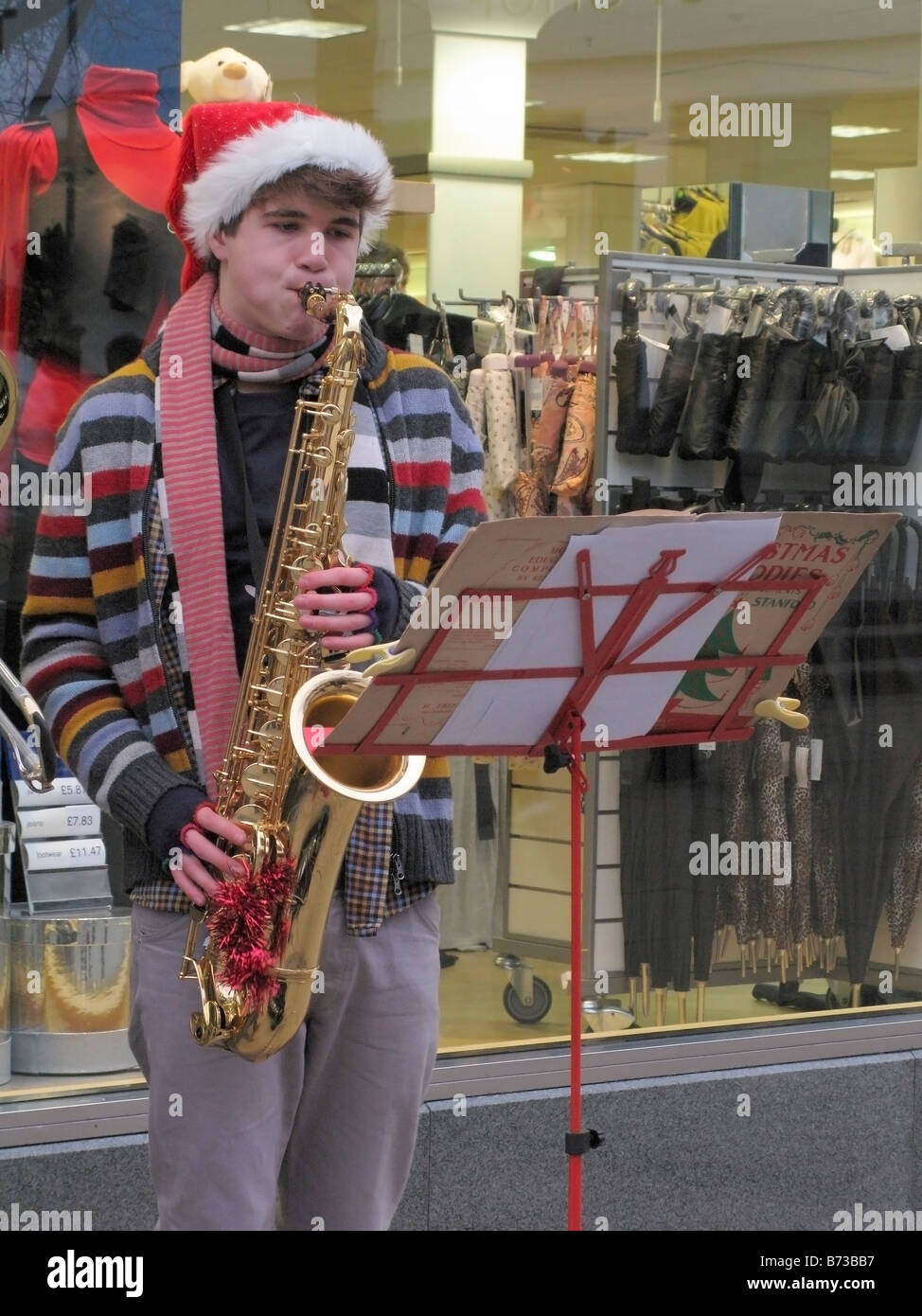 A lad busking money by playing Christmas carols on trombones on the Street of Norwich during Christmas period Stock Photo