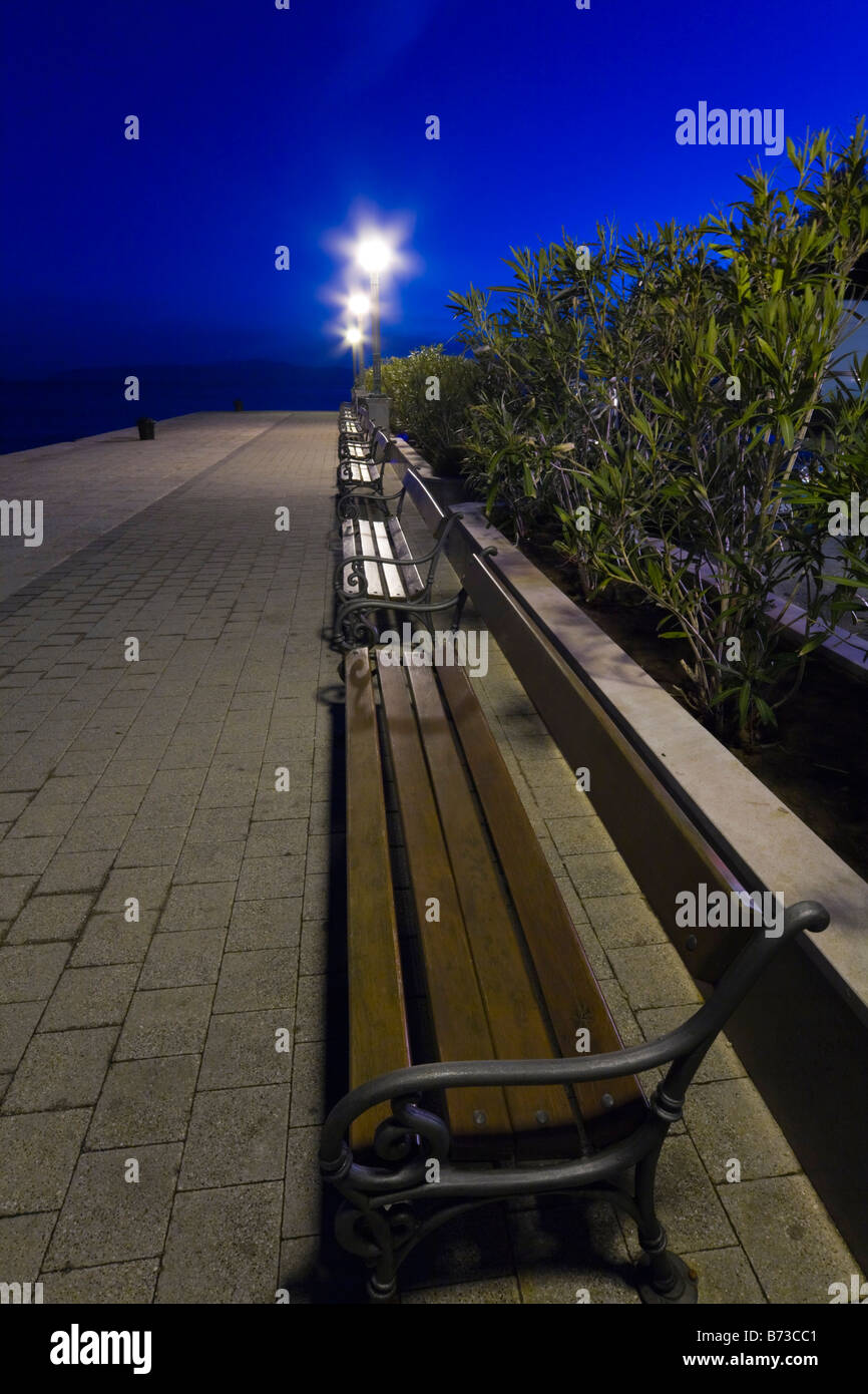 Park benches lined on sea promenade, vacated at midnight, Lovran in Croatia Stock Photo