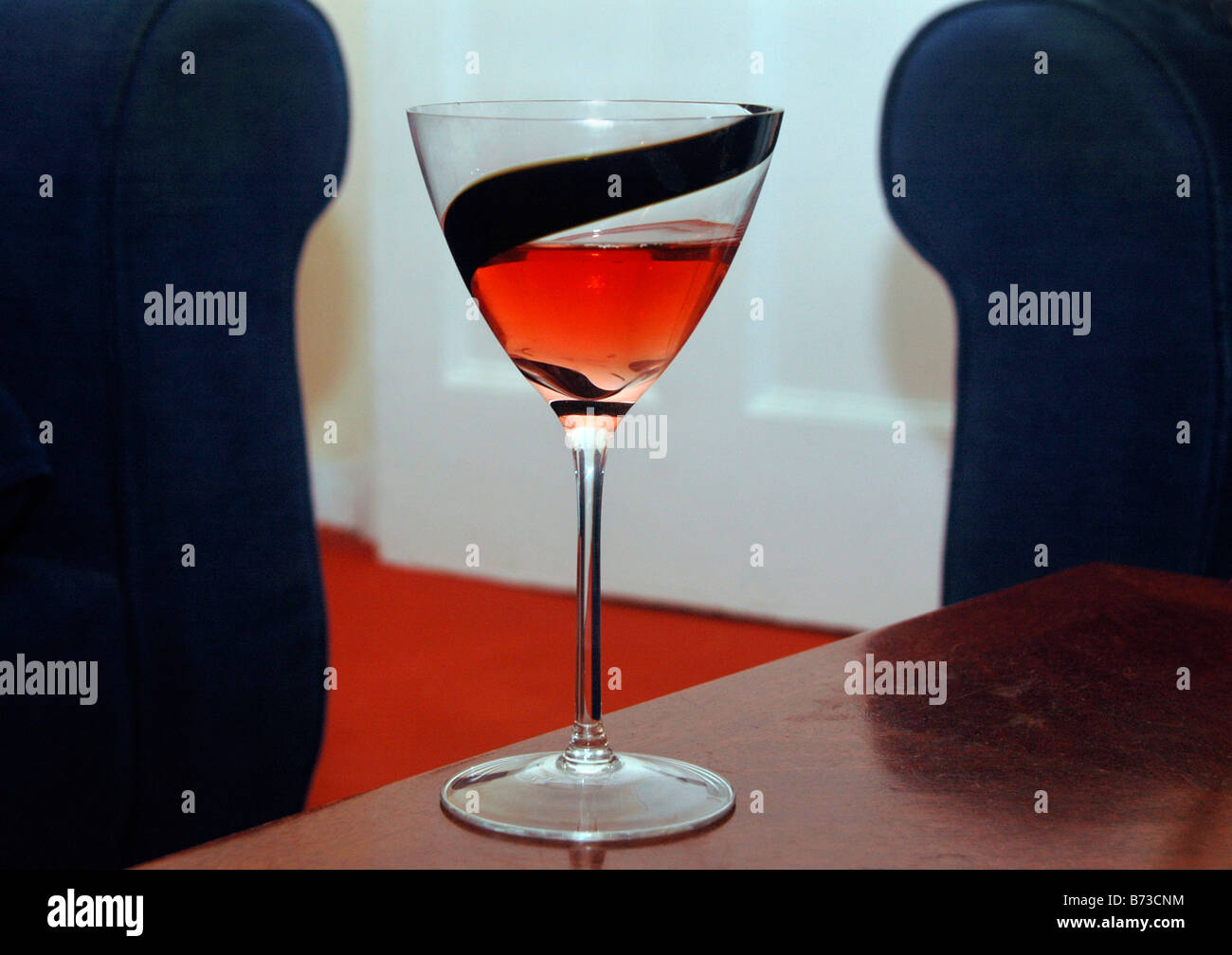 A glass of rose wine sits on a table framed by 2 armchairs. Stock Photo