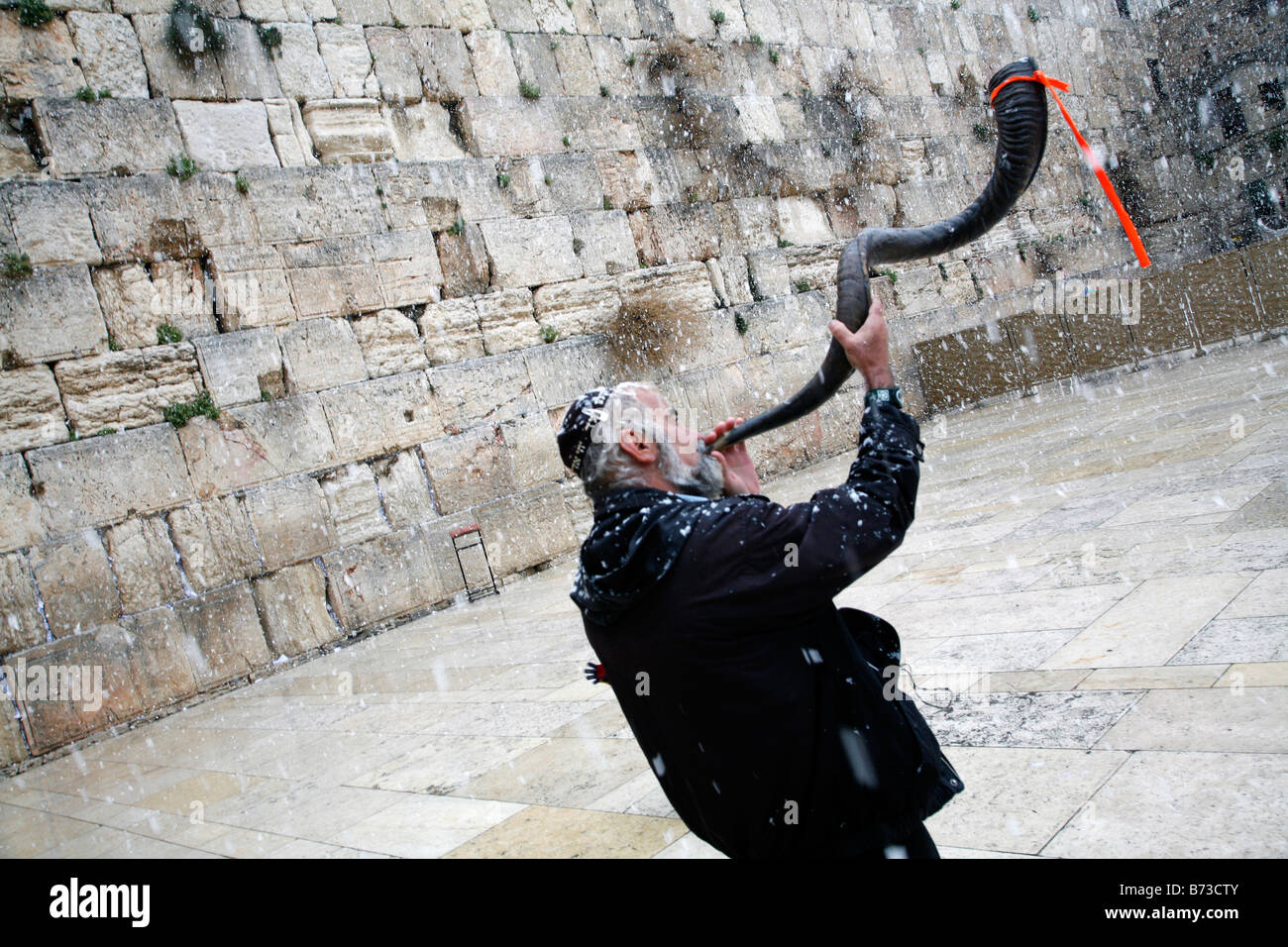 A religious Jew blowing a shofar at the Western Wall in in the Old City of Jerusalem during a snow storm. Stock Photo