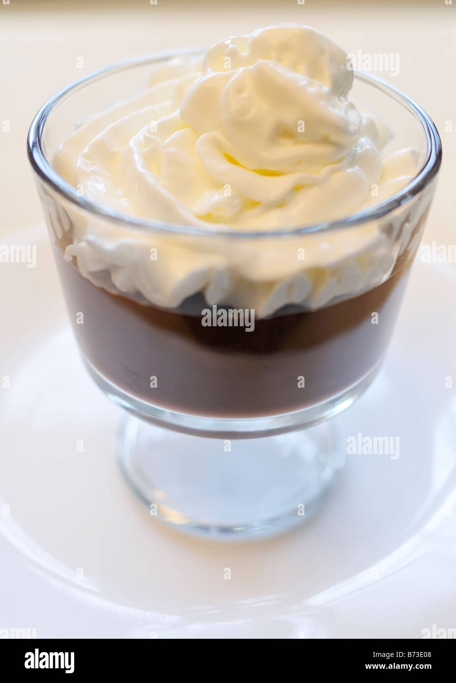 Chocolate pudding topped with whipped cream in a glass dessert bowl on white background. Stock Photo