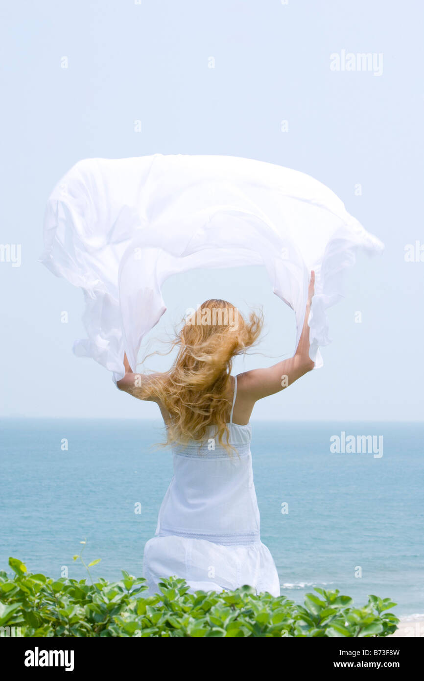 Young woman standing holding out shawl in wind rear view Stock Photo