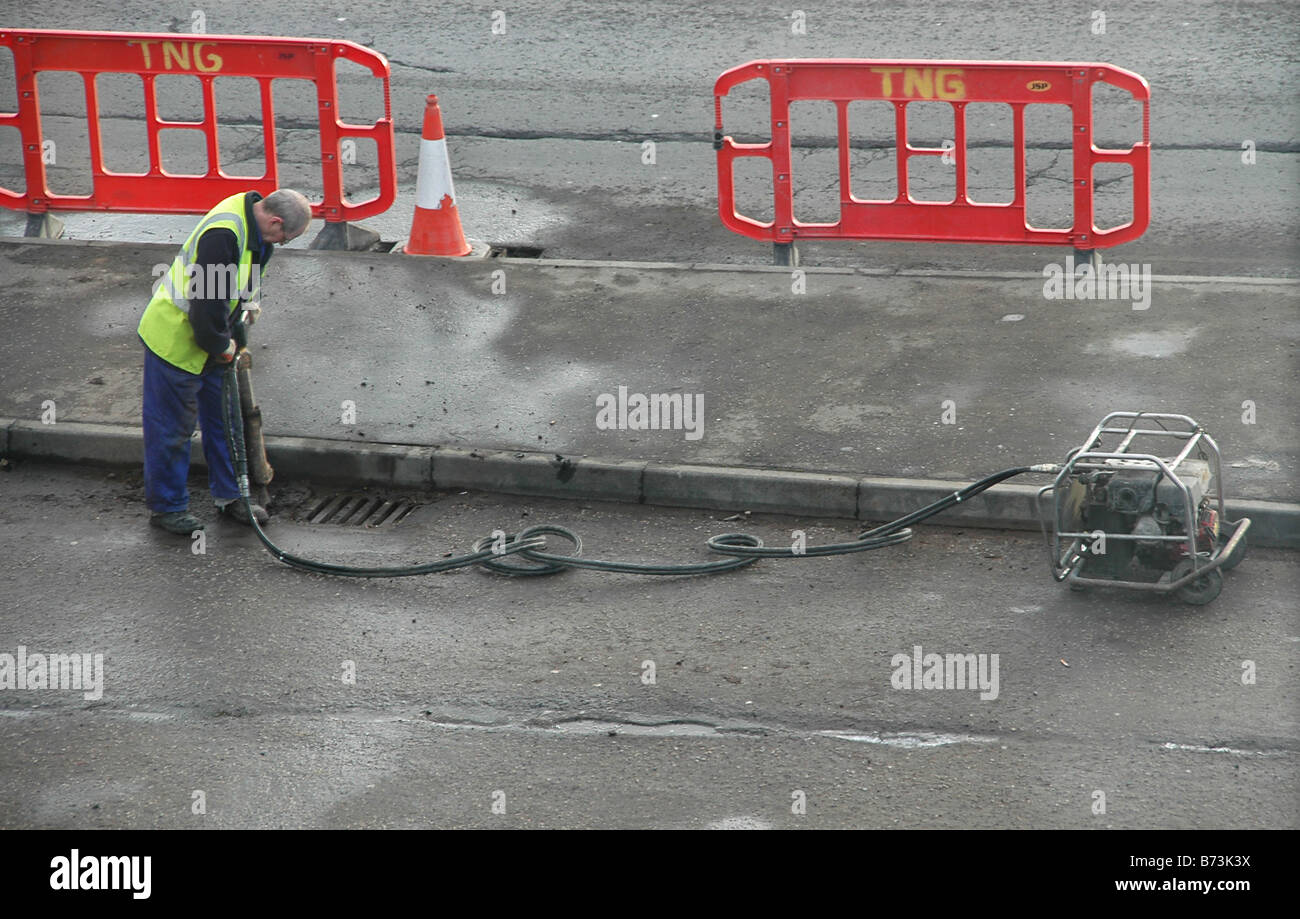 a workman uses a pneumatic drill on a section of coned off road. Stock Photo