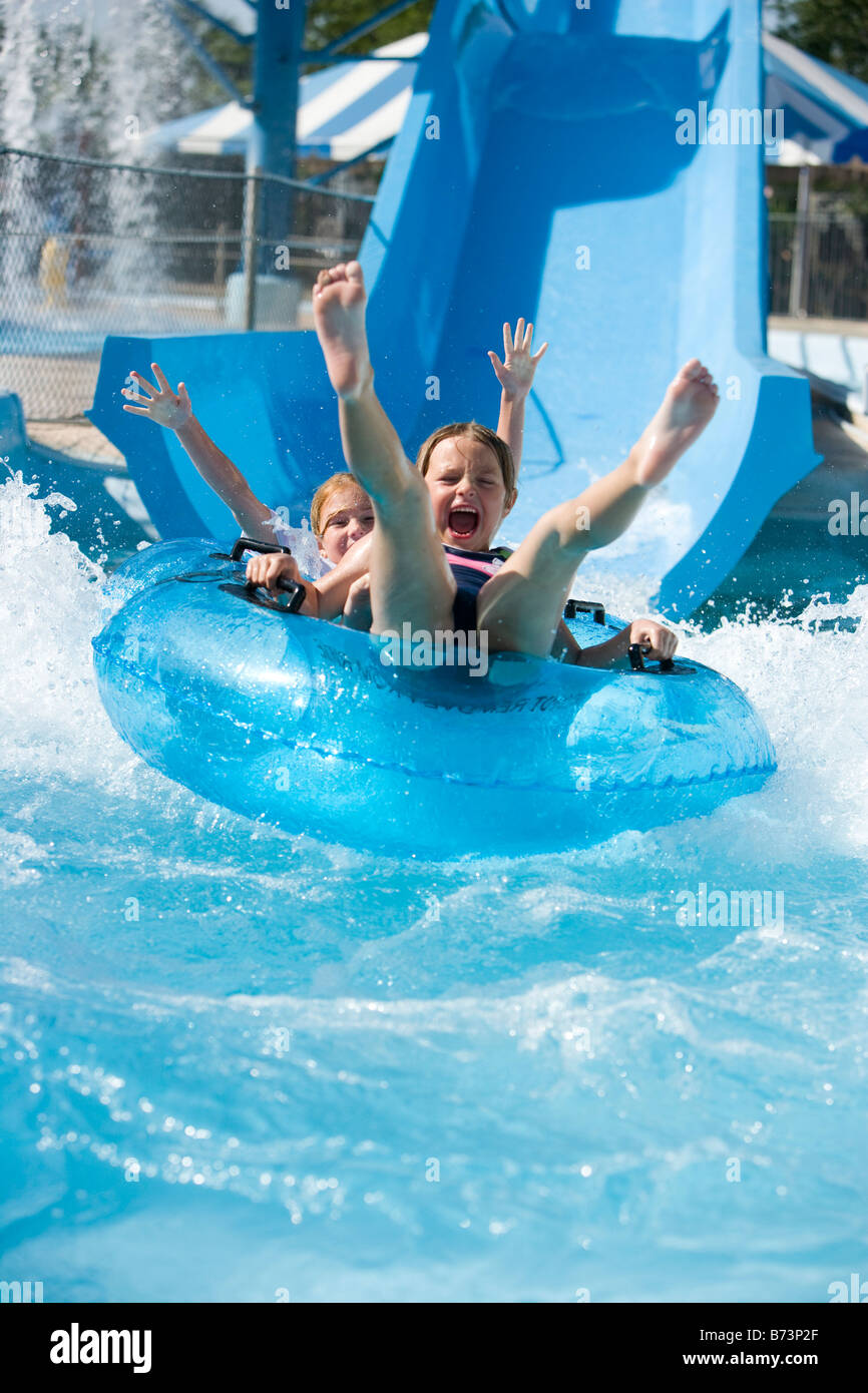 Portrait of girls sliding down waterslide together on innertube in water park Stock Photo