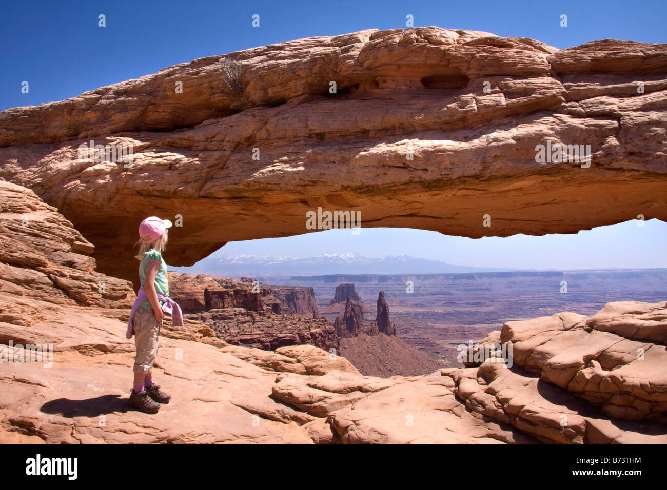 A little girl enjoys the view thru Mesa Arch in the Island of the Sky district of Canyonlands National Park Utah Stock Photo