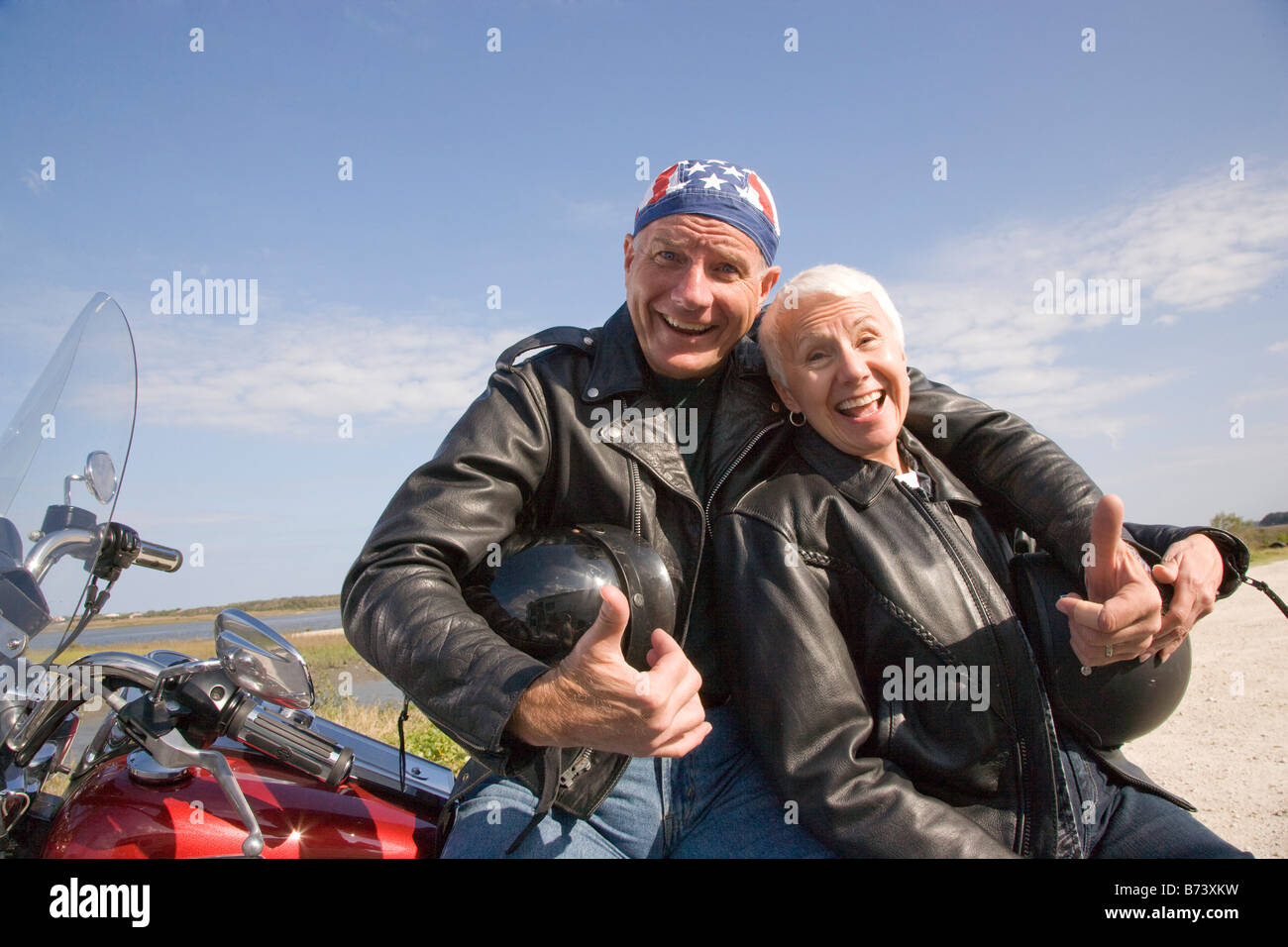 Happy senior biker couple sitting leaning against 