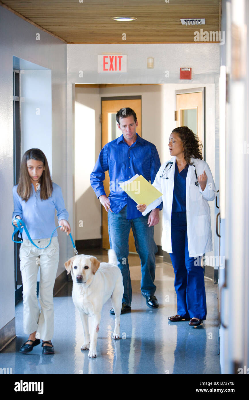 Veterinarian walking with family and dog down clinic corridor Stock