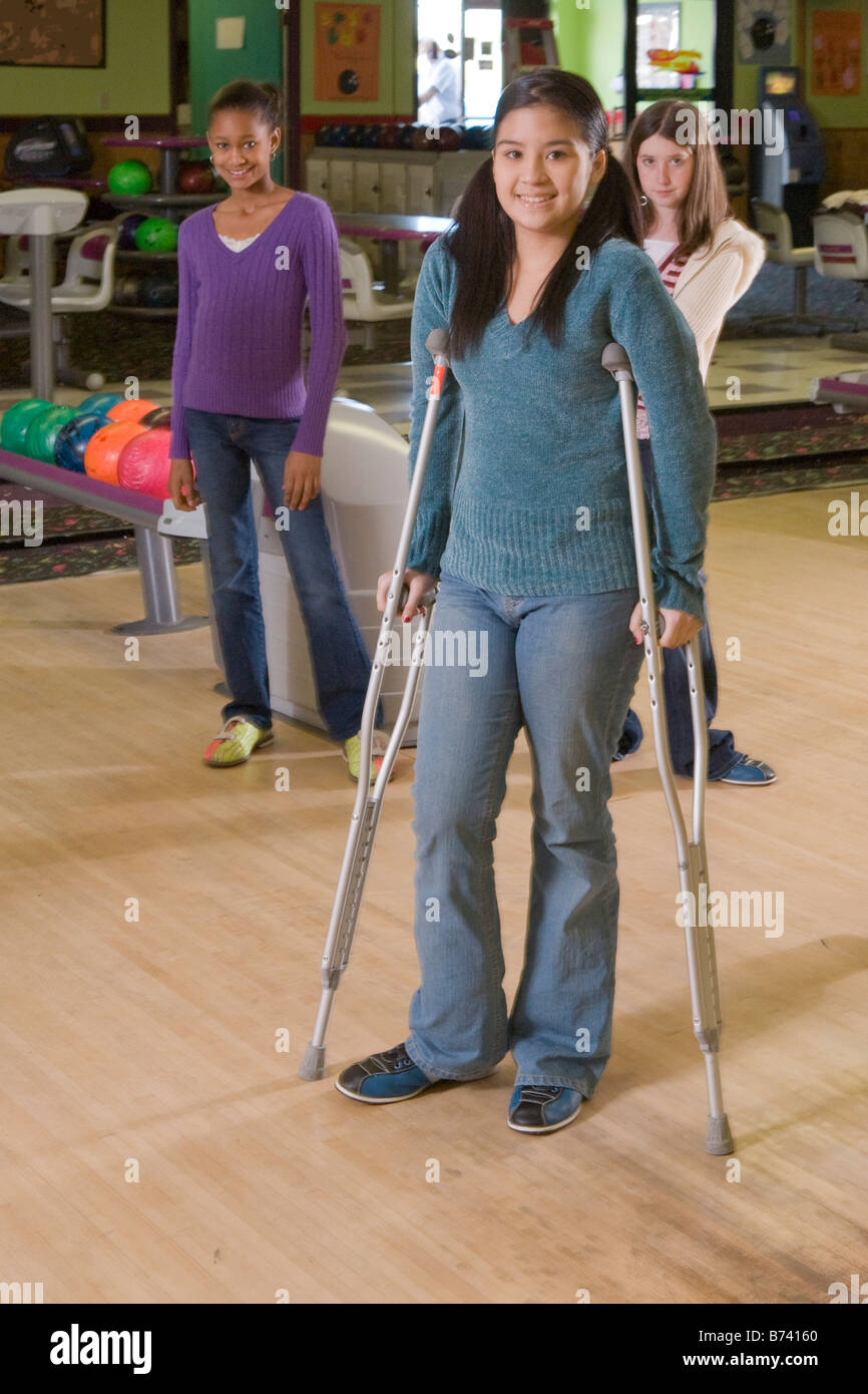Asian teenage girl on crutches with friends in bowling alley Stock