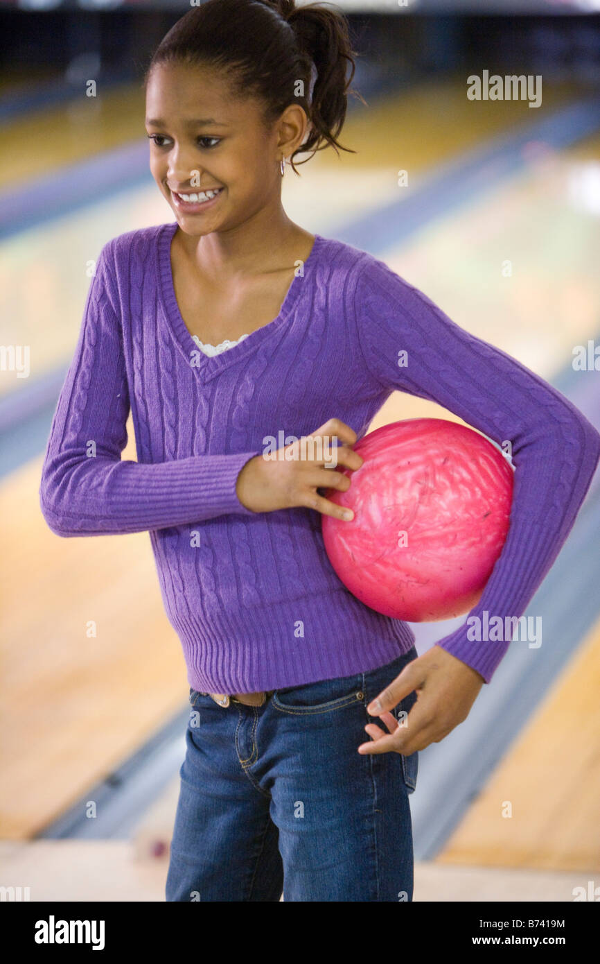 Happy African American preteen girl holding bowling ball in bowling
