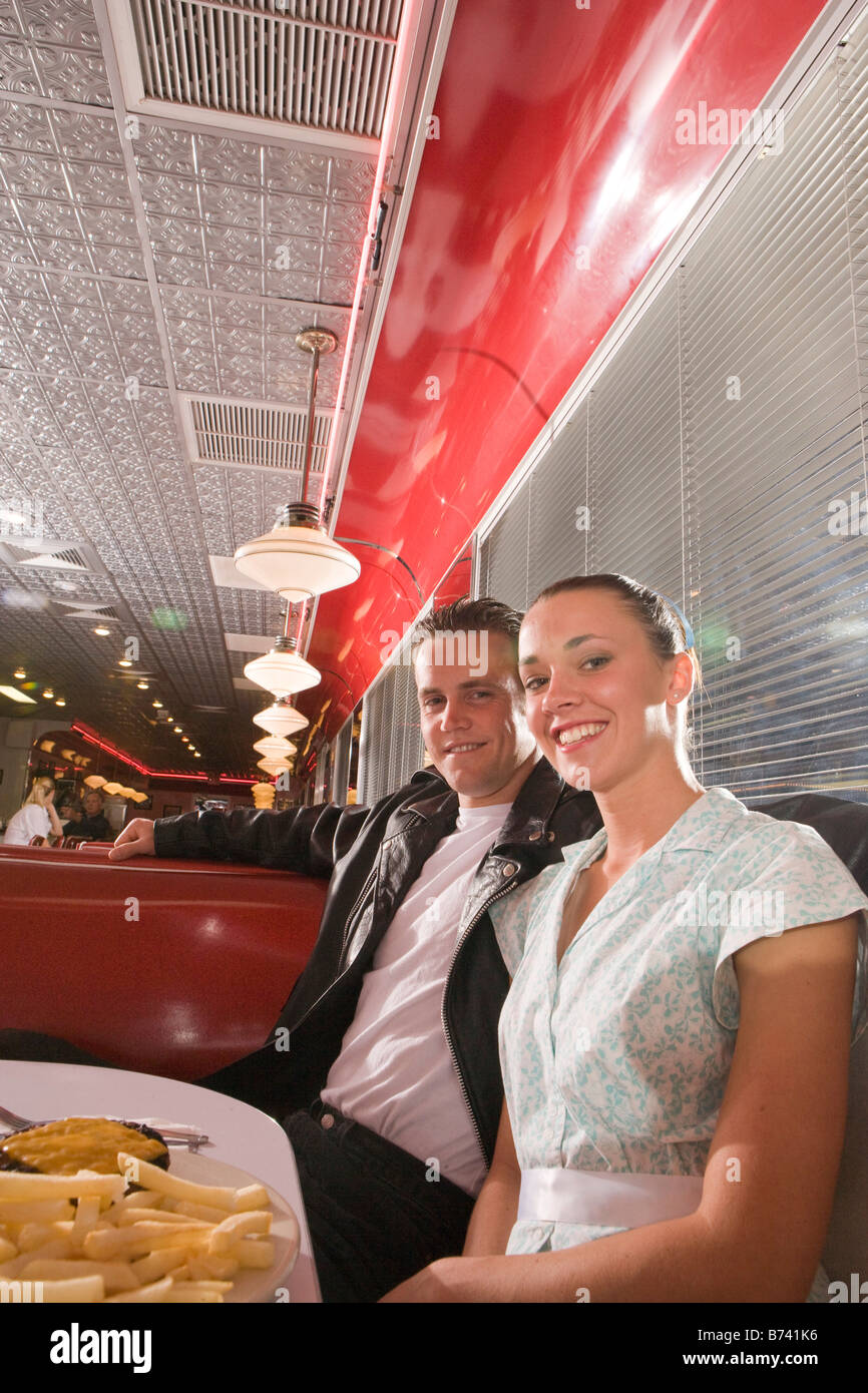 Young couple in 1950s style clothing in diner eating burgers and fries Stock Photo