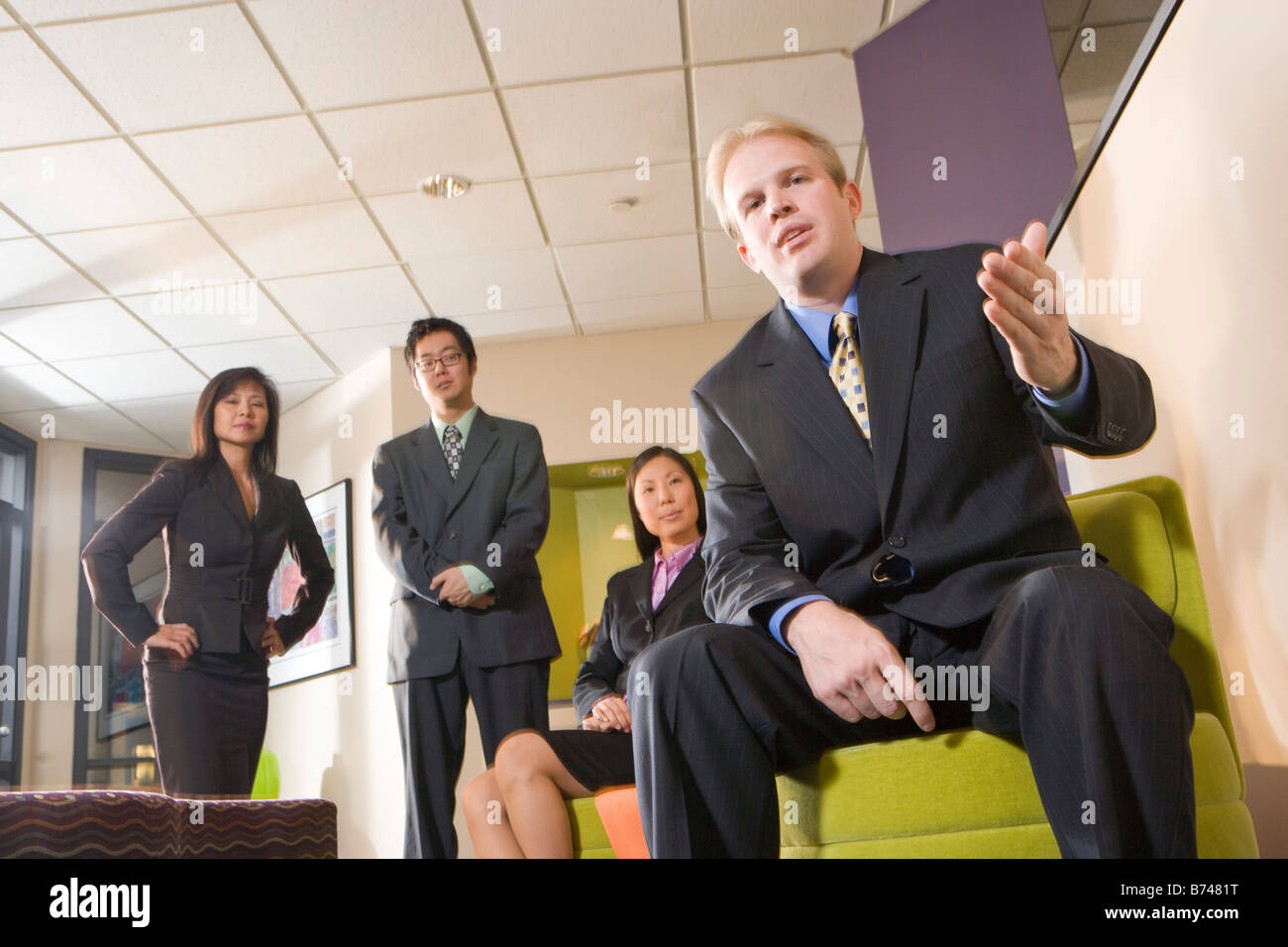 Caucasian businessman waiting in lobby with three Asian executives Stock Photo