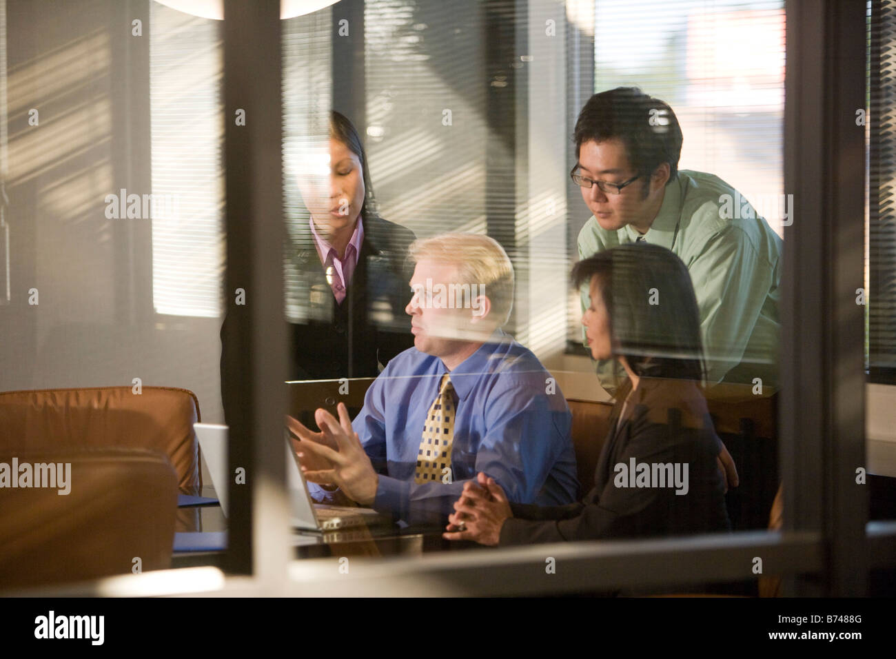 Caucasian businessman on laptop with group of Asian businesspeople Stock Photo