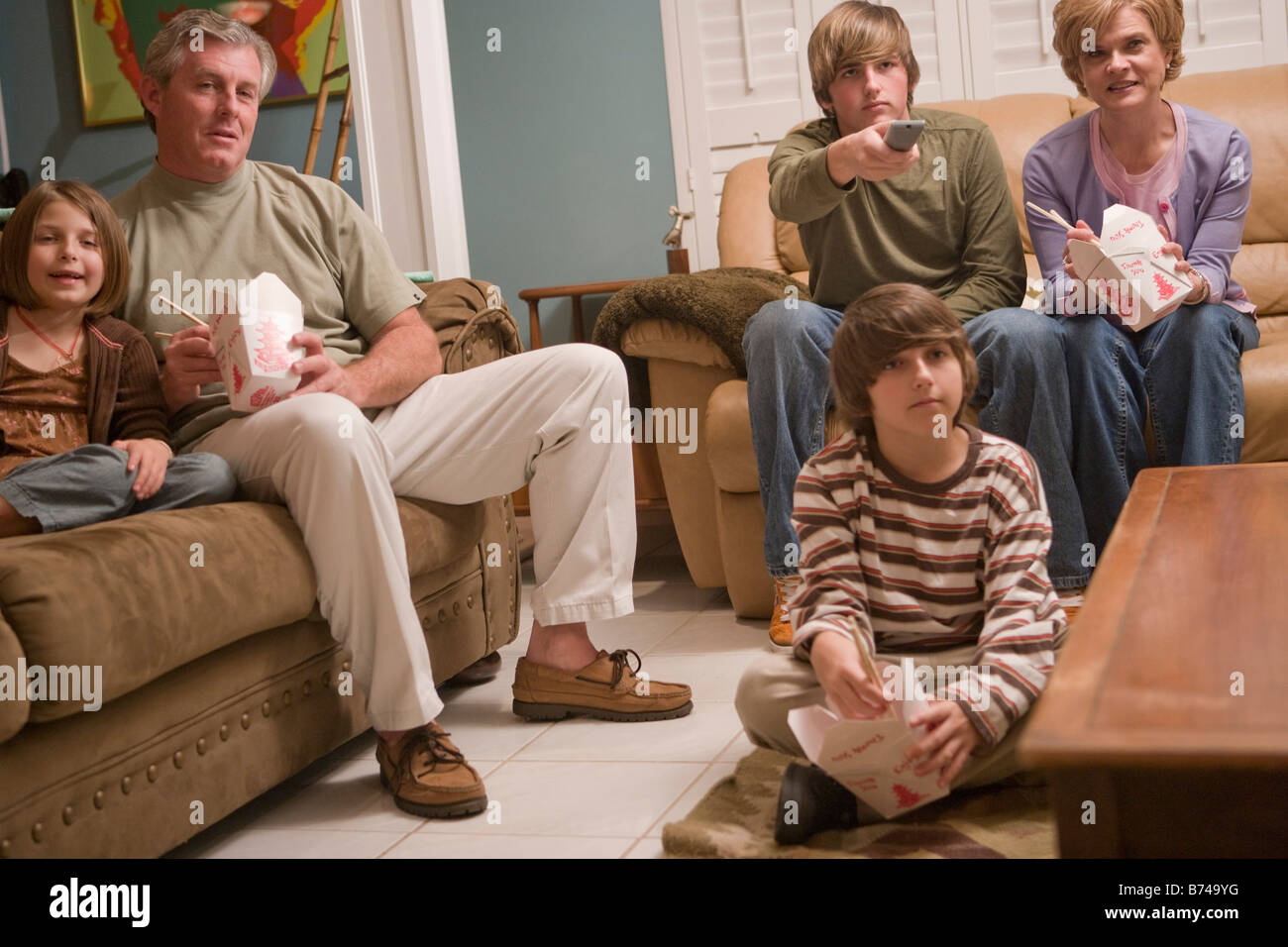 Family eating Chinese takeout dinner on couch watching TV Stock Photo