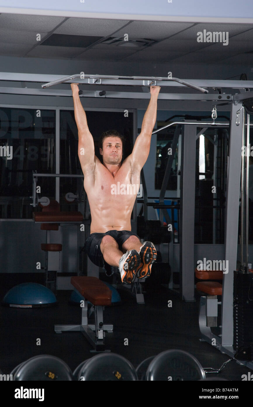Young man hanging on rod in gym with exercising equipment in