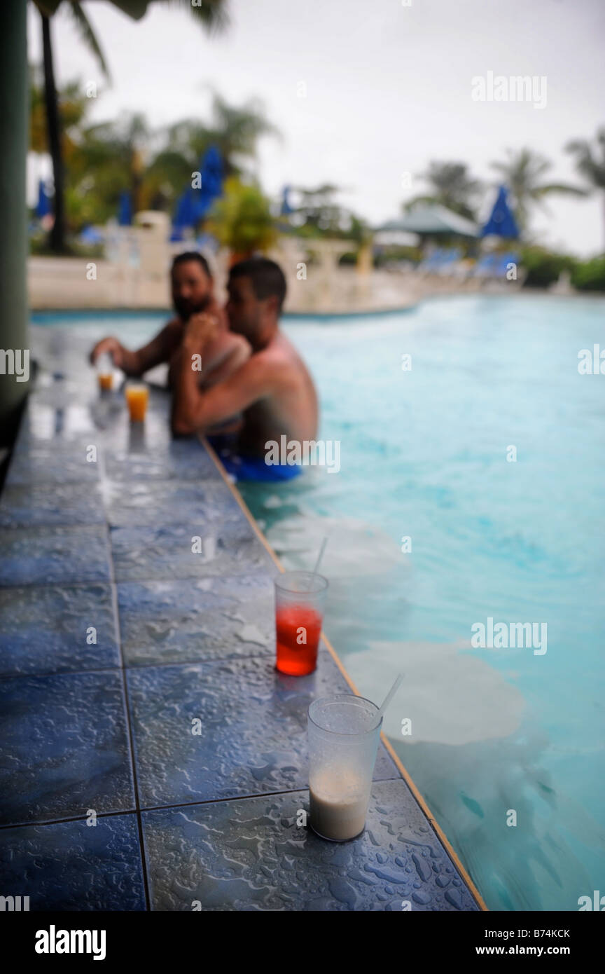 TWO TOURISTS SIT AT THE POOL BAR DURING A RAIN STORM AT A CARIBBEAN HOLIDAY RESORT Stock Photo
