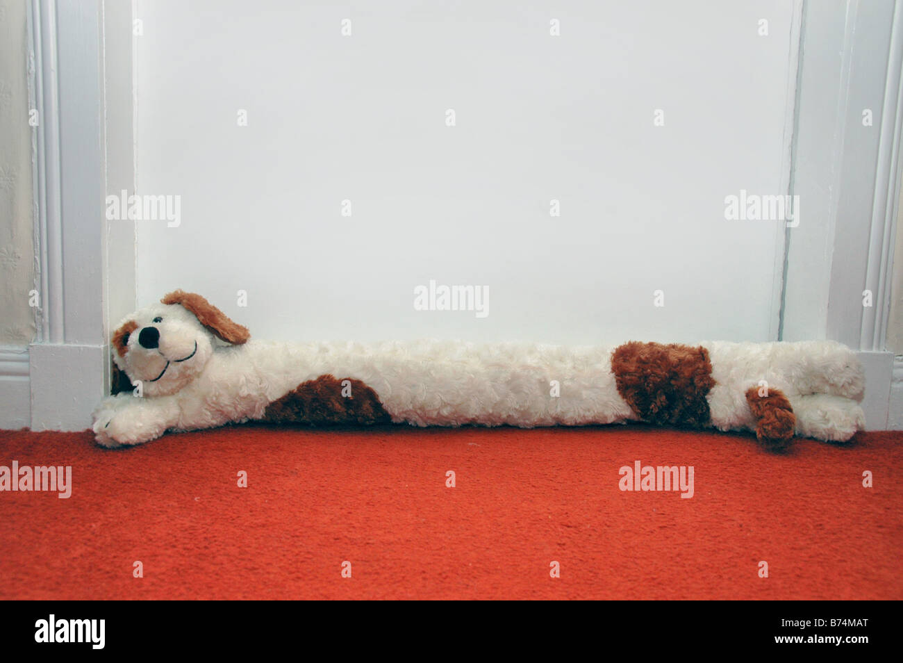 A dog shaped draft excluder lies at the base of a door. Stock Photo