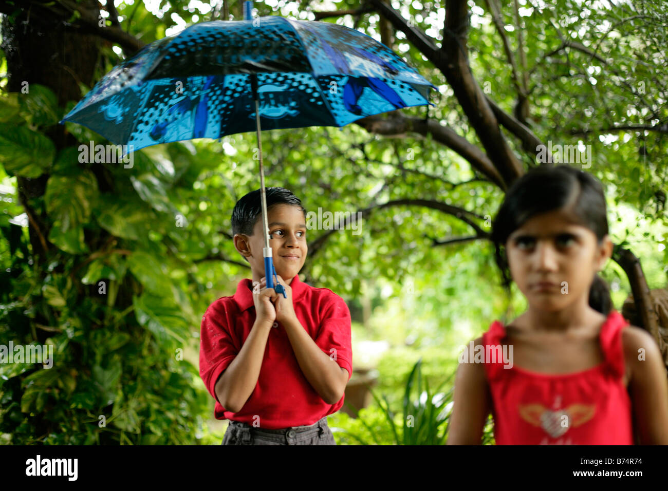 Mischievous young boy happily holding an umbrella while an unhappy girl looks on the foreground focus is on the boy Stock Photo