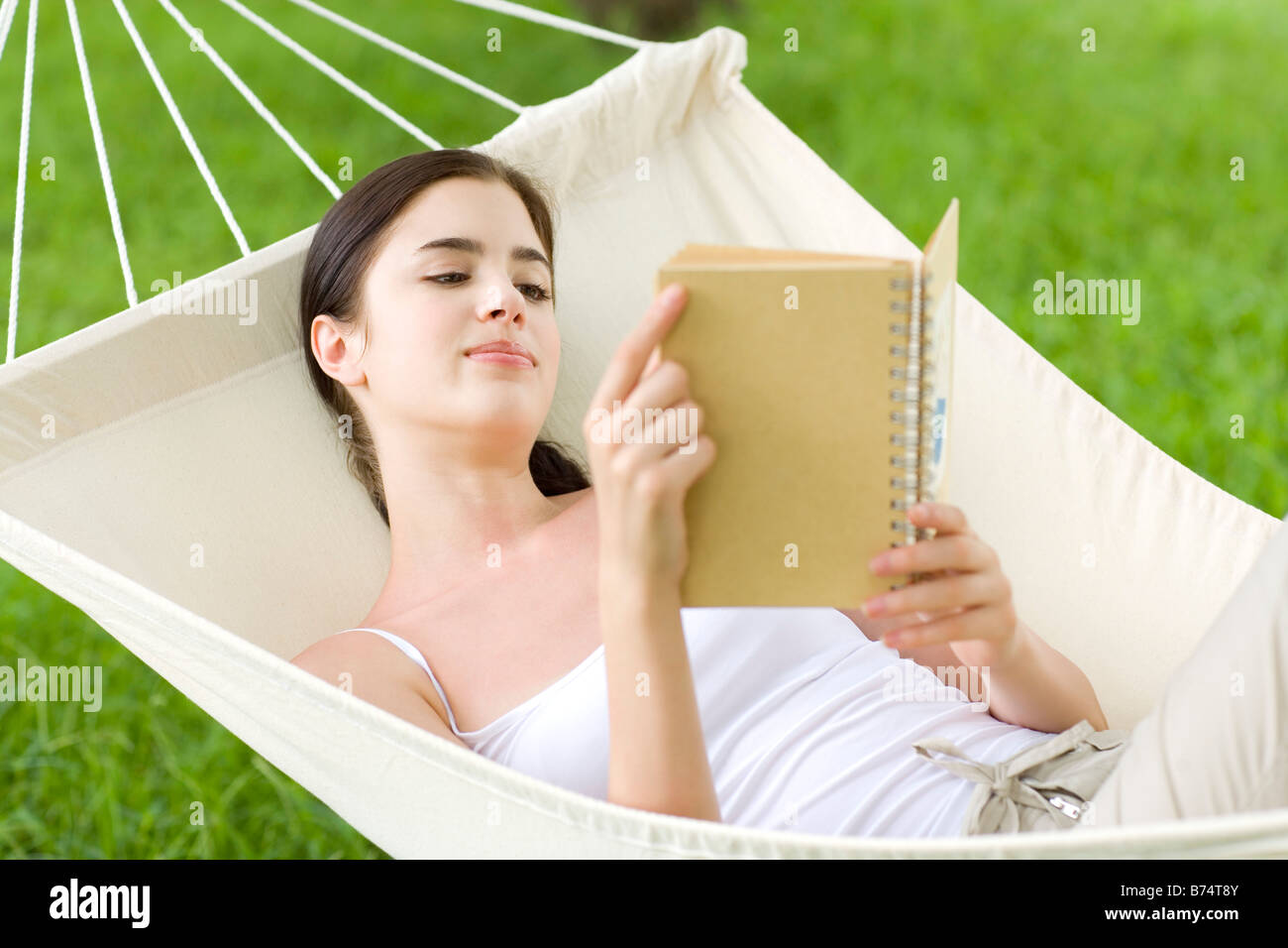 Young woman lying in hammock reading book Stock Photo - Alamy