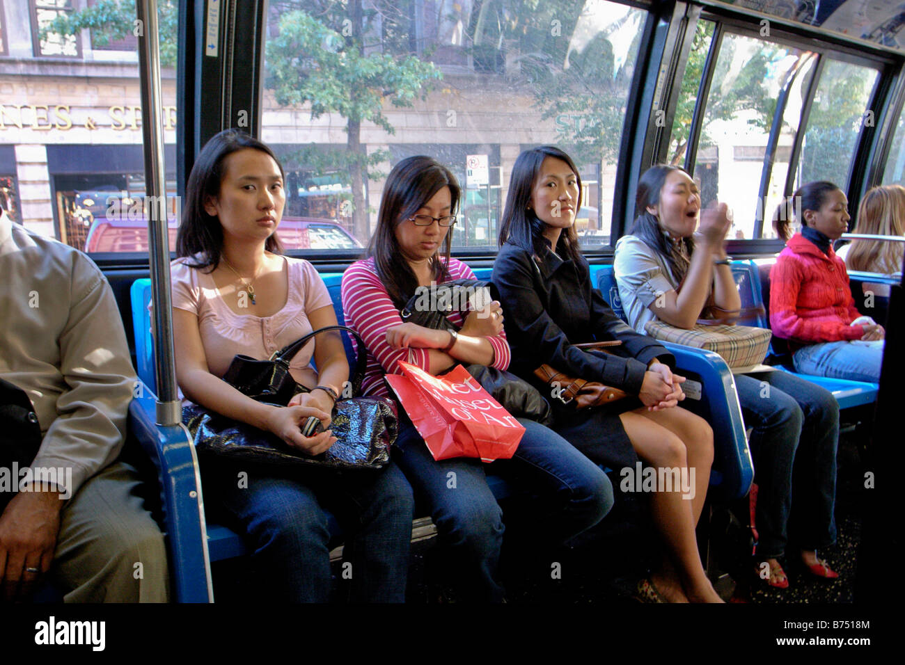 Asian and African American women ride a Fifth Avenue bus in NY City Note woman sneezing at right Stock Photo