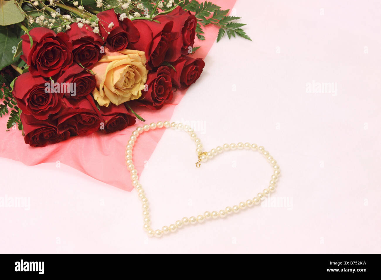 Still life of red roses with one yellow rose in center and a pearl necklace in the shape of a heart on white background Stock Photo