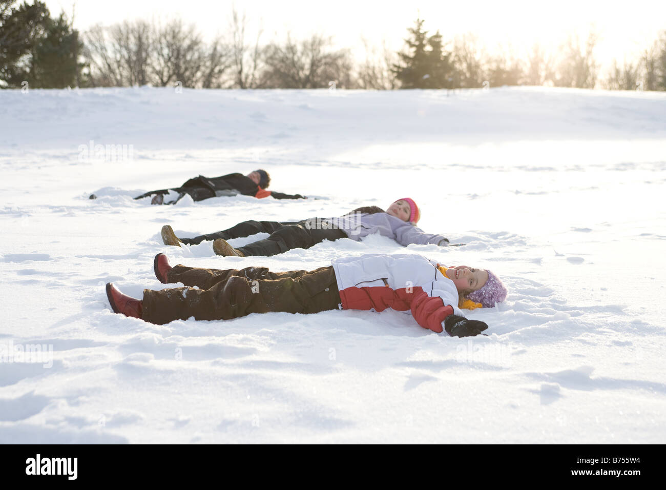 3 kids, (14, 13, and 9 years old) lying on snow, making snow angel, Winnipeg, Canada Stock Photo