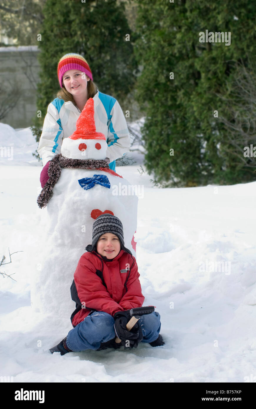 Young girl and boy beside snowman, Winnipeg, Canada Stock Photo