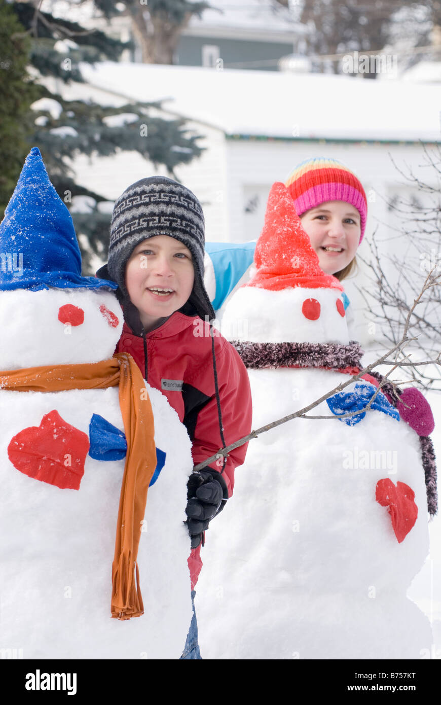 Young boy and girl standing behind snowmen, Winnipeg, Canada Stock Photo