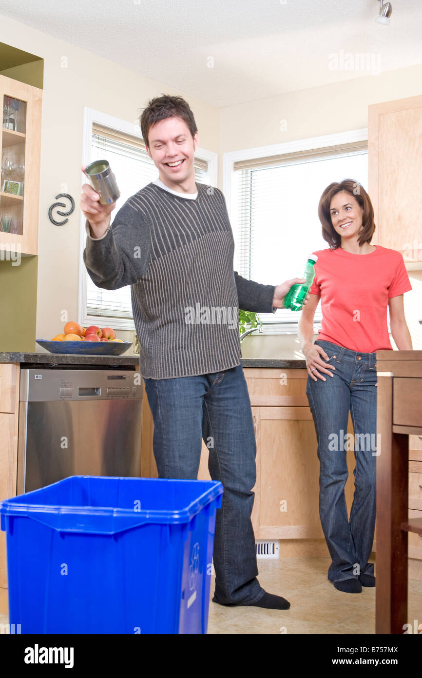 Couple laughing in kitchen as man tosses can into recycling bin, Winnipeg, Canada Stock Photo