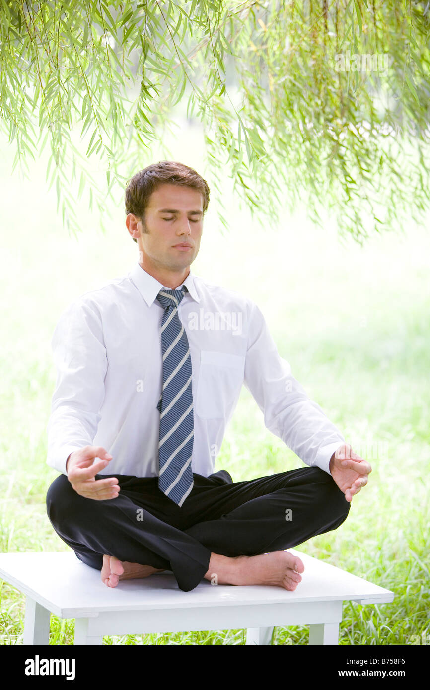 Businessman in lotus position sitting on desk eyes closed Stock Photo