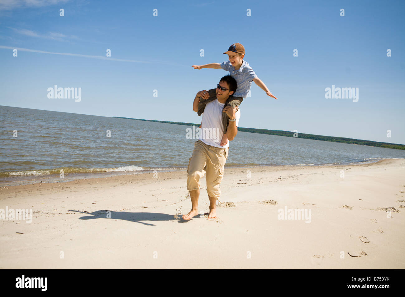 Man carries boy (7) on his shoulders as boy holds arms out, Grand Beach Provincial Park, Manitoba, Canada Stock Photo